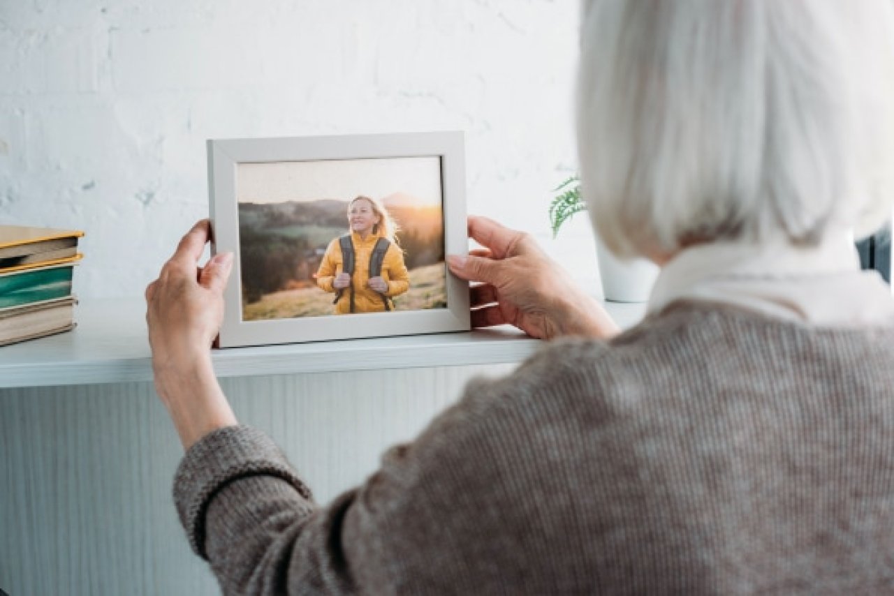 Eldre dame plasserer et innrammet portrettbilde av en dame i hyllen.